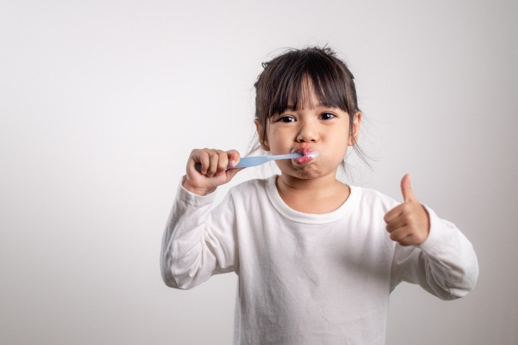 Young girl brushing her teeth and giving a thumbs up