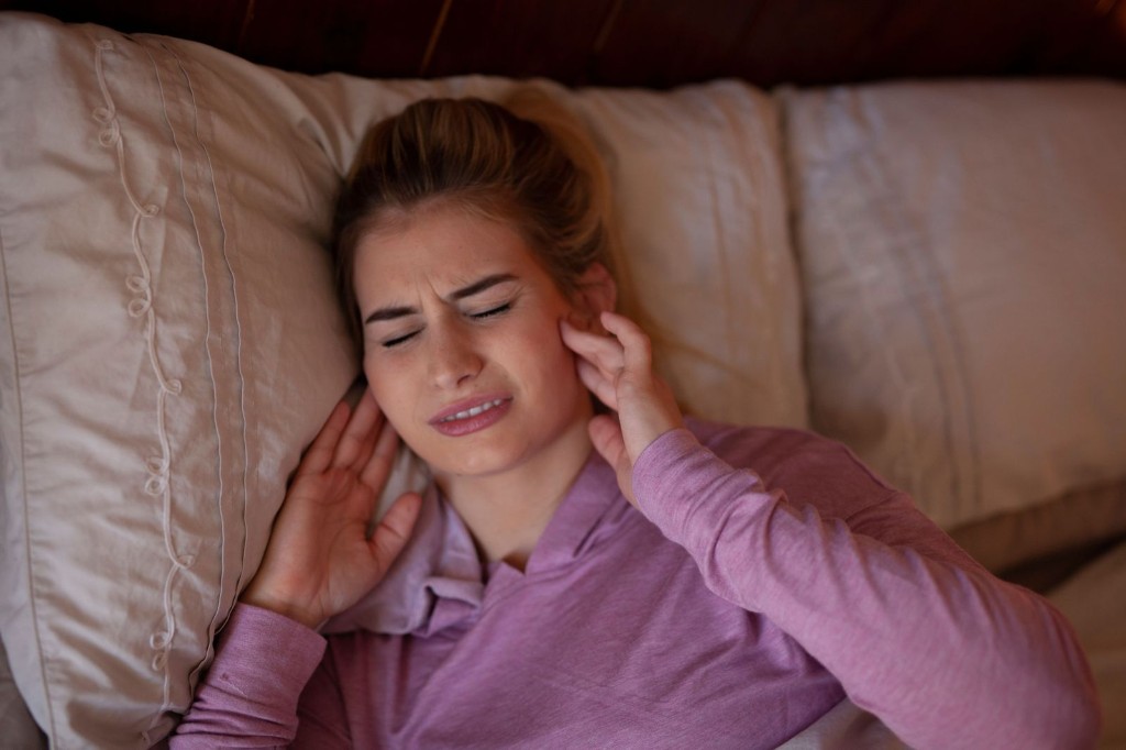 Woman in bed holding her jaw in pain from teeth clenching and grinding