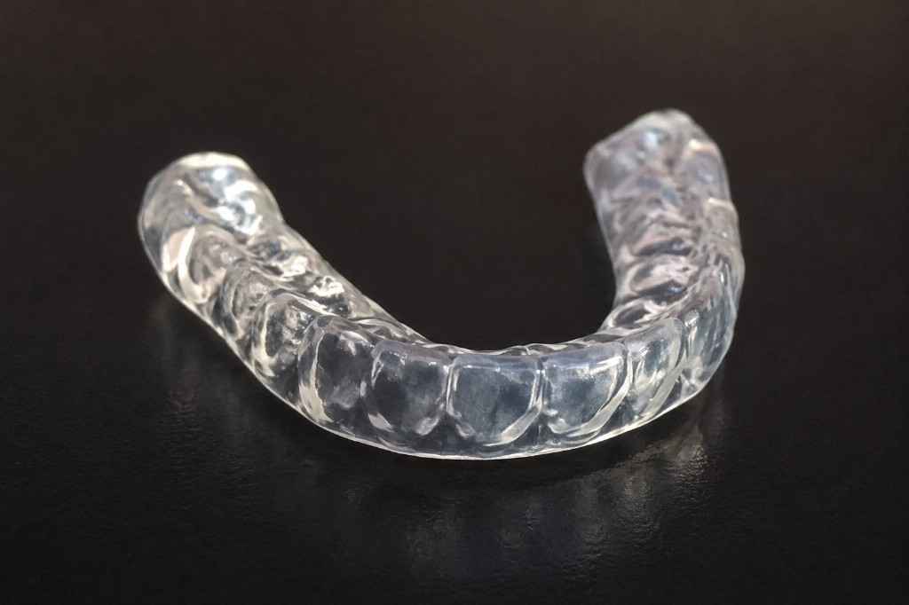 Clear custom-fitted dental mouthguard on a dark studio background