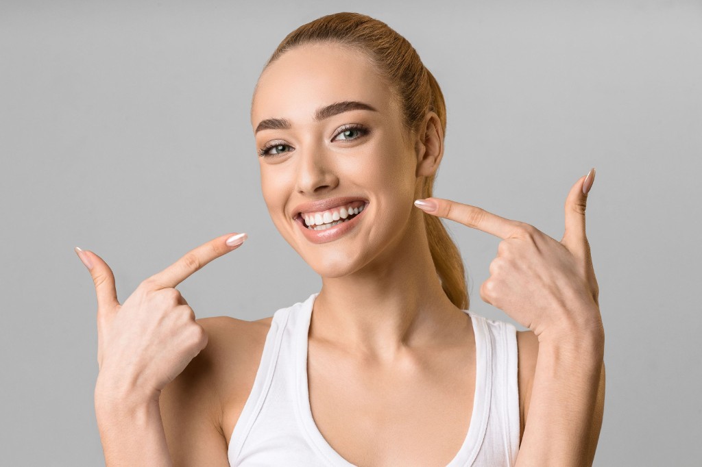 Woman smiling and pointing to bright white teeth